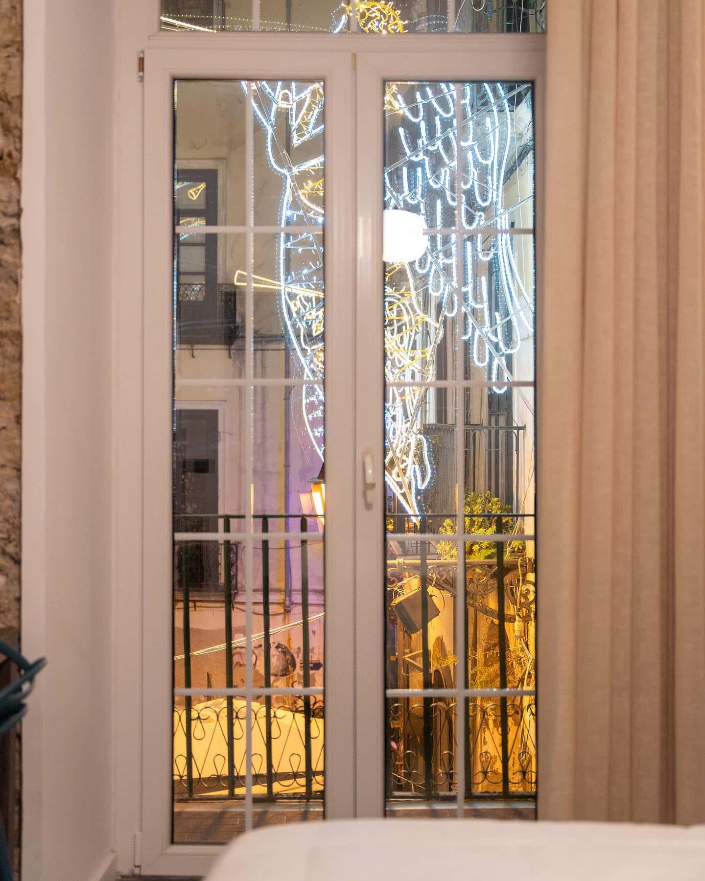 Le portefinestre di una camera, con gli angeli luminosi di Via Duomo visibili dal balcone