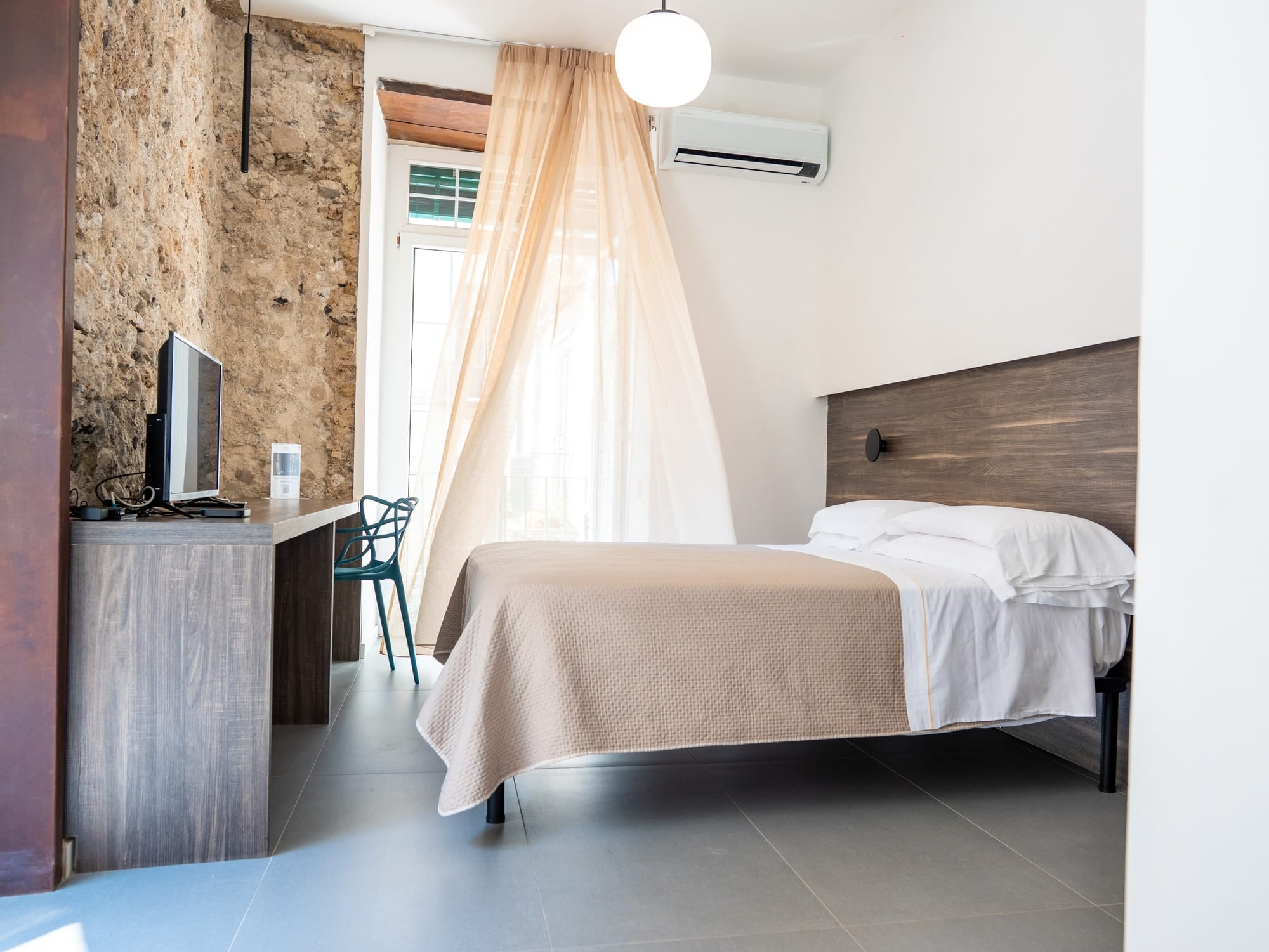 Gea by day: the bed, the desk and the light curtain in front of the French window, beside the stone wall