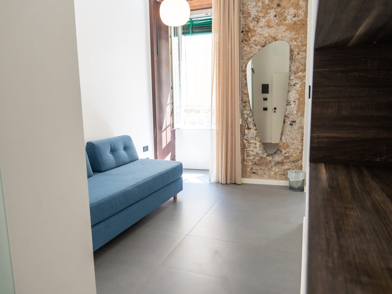 The blue sofa in Gea, with the mirror on the stone wall and the French window