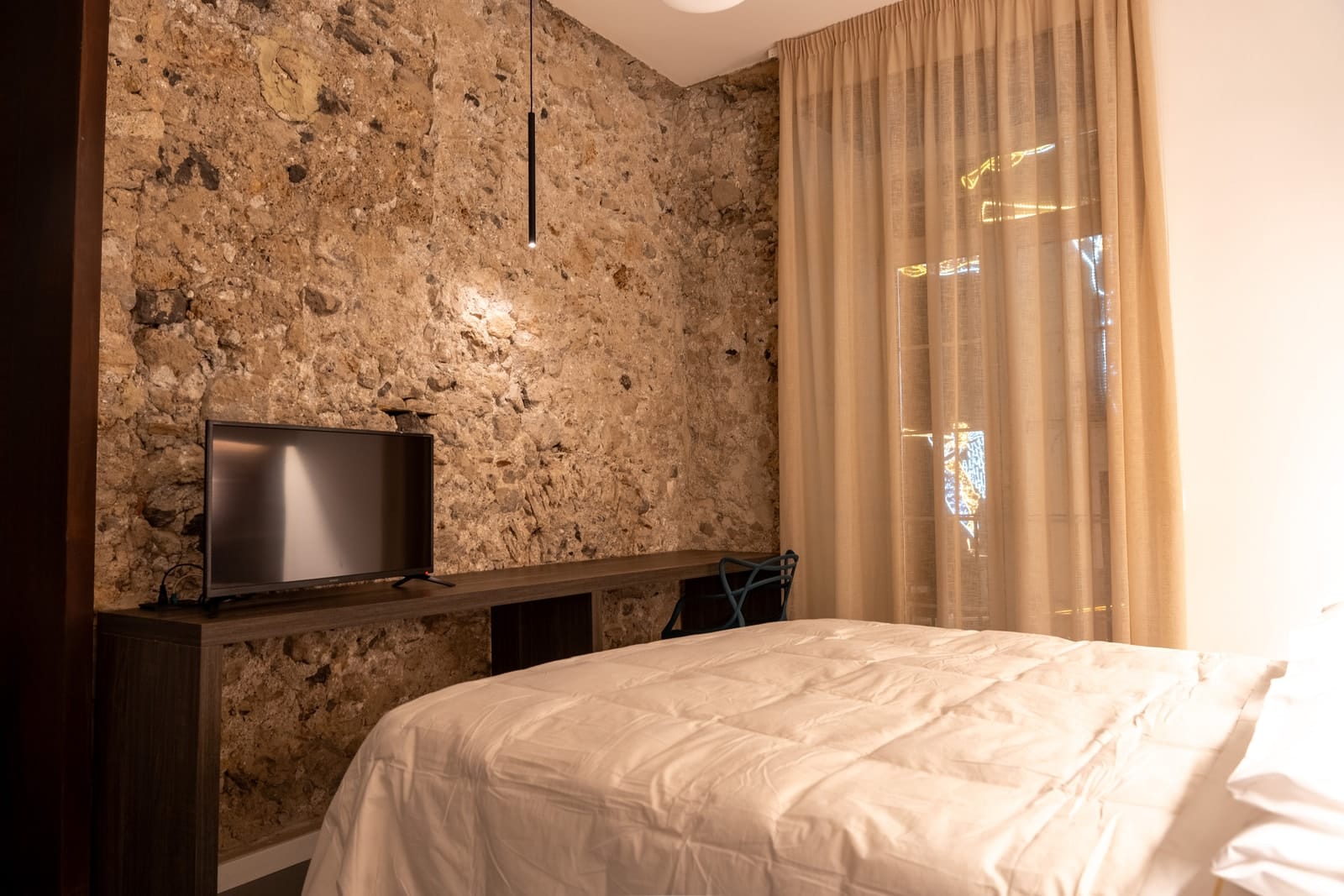 The bare stone wall in Gea, with the television on the desk and the curtain at the French window