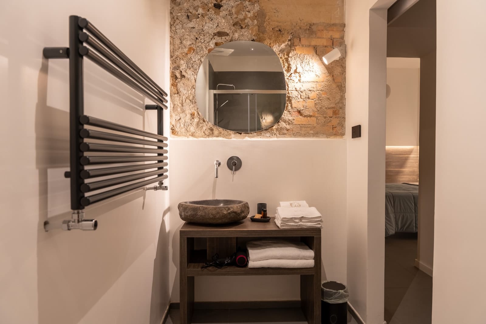 The bathroom in Hera: the stone basin under the mirror on the stone and brick wall, and the room through the door