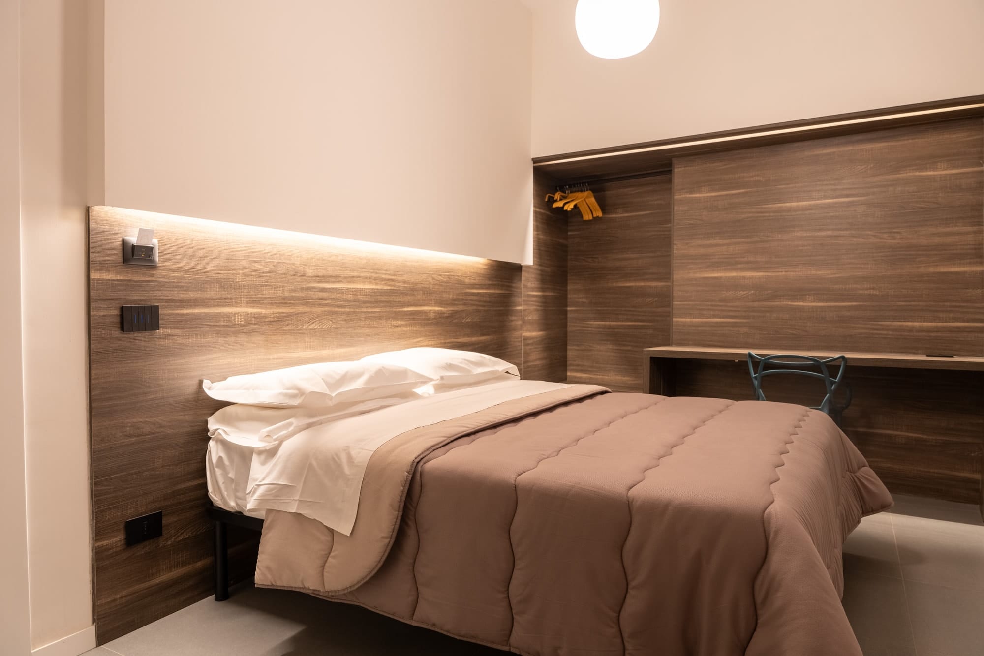 Hestia: the bed, the wooden wall with its hidden light, the desk and the wardrobe