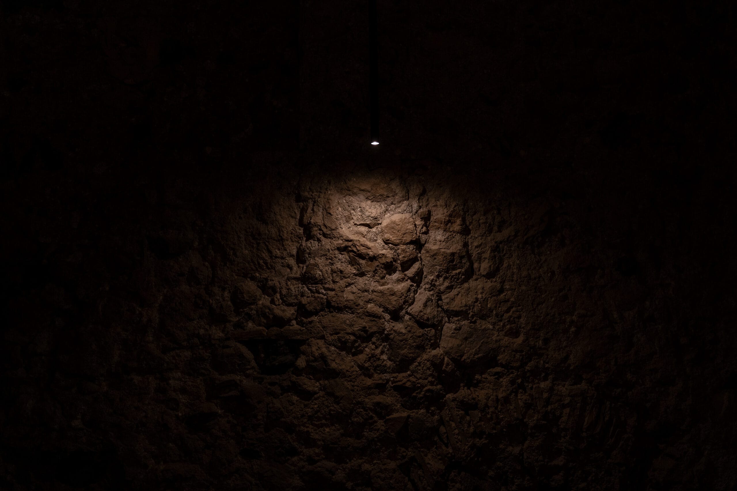 A bare stone wall lit by a single pendant lamp, in the dark