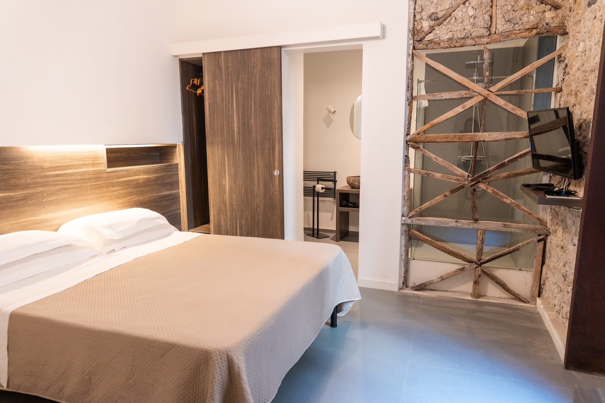 La camera Zeus: il letto con la testiera di legno, la porta scorrevole e la parete della doccia con i controventi di legno a vista