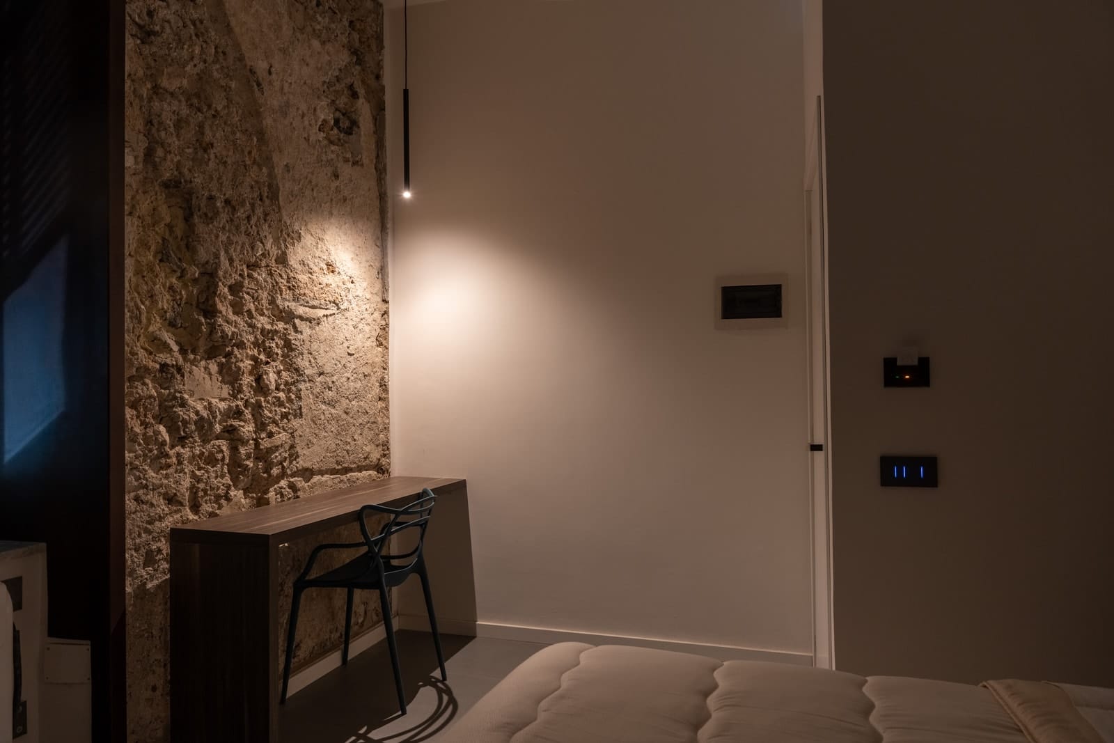 L’angolo della scrivania nella camera Zeus, contro il muro di pietra illuminato da una lampada a sospensione